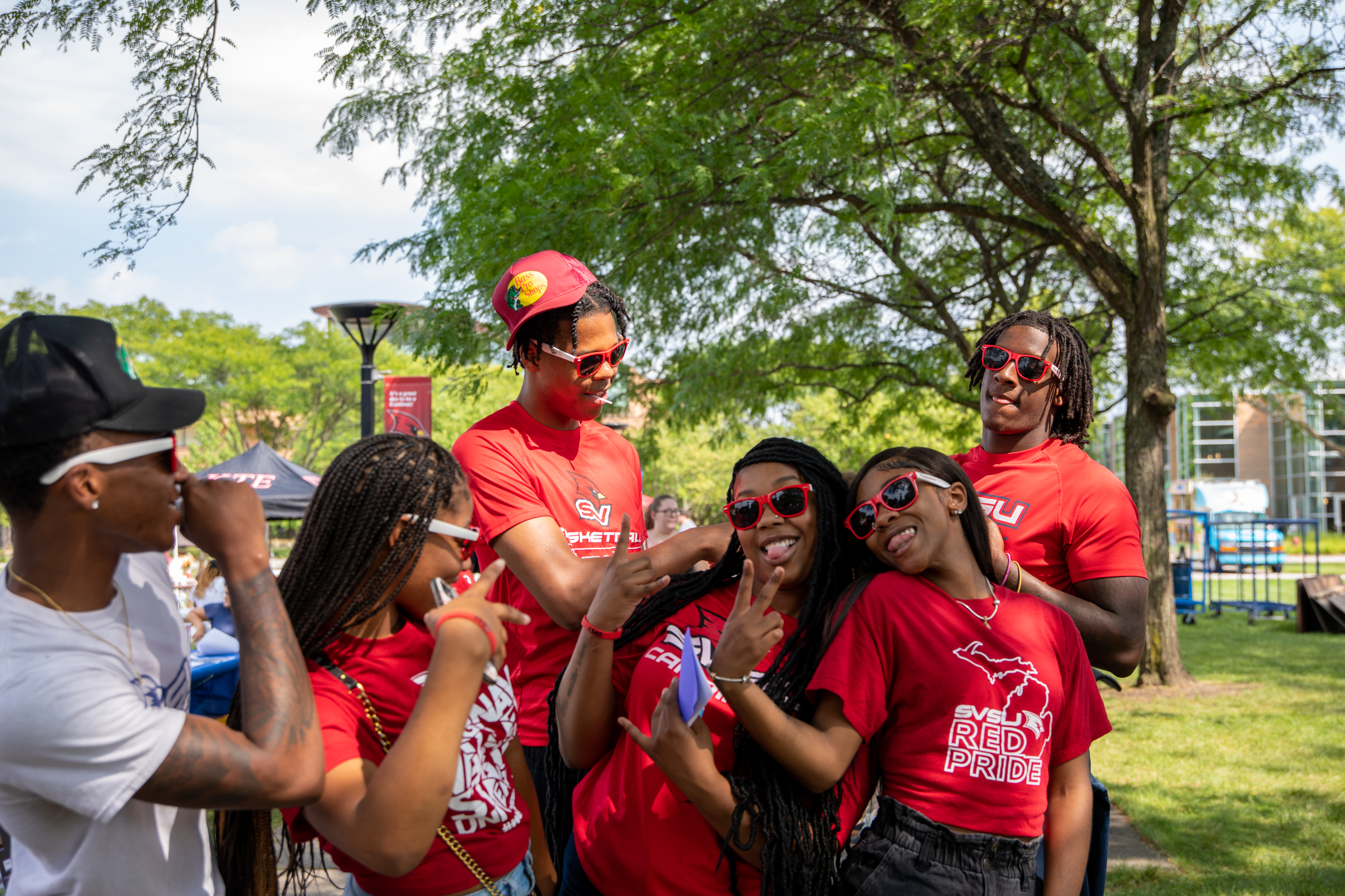 Students posing for a photo together at the SVSU Red Pride Picnic wearing SVSU Sunglasses and showing the peace sign.